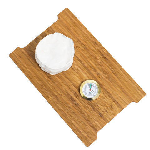 overhead view of small white bloomy rind cheese with analog hygrometer on wooden board with white background