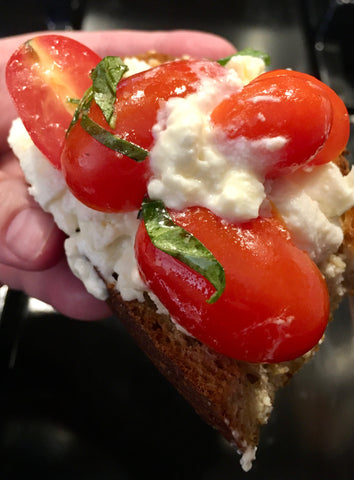 closeup of bread covered with burrata cheese and grape tomatoes with basil