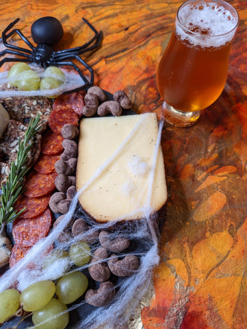 closeup of cheese, cocoa cashers, grapes, charcuterie on halloween cheese board with beer and fake spider 