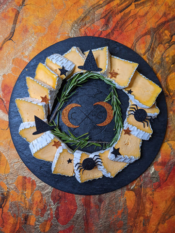 black cheese board with orange soft ripened cheese decorated for halloween