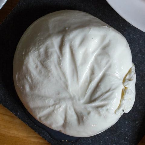 overhead view of round white ball of homemade burrata on slate