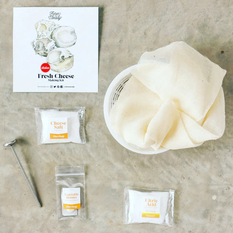 overhead view of home cheesemaking kit with labeled bags of salt, citric acid, rennnet, and tools for cheesemaking