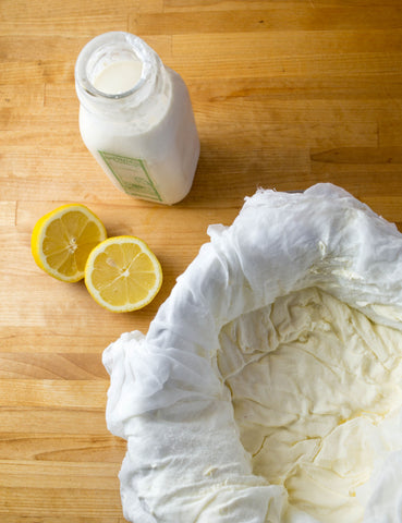 overhead view of milk, cut lemon, and bowl of cheesecloth and cheese curds n wooden counter 