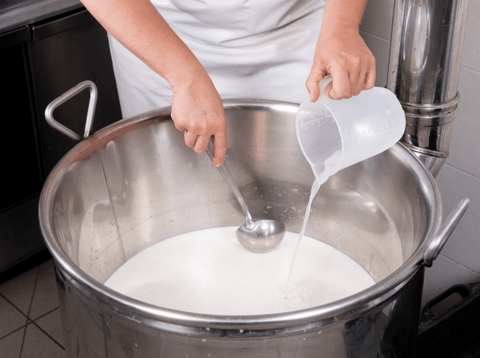 cheesemaker stirring rennet from home cheesemaking kit into large pot of milk