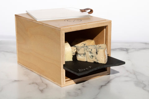 wooden box containing blue cheese wedges on black slate on marble countertop in front of white background