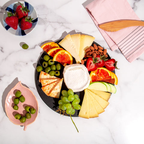 circular slate serving board styled with cheese, fruit, and olives on marble table