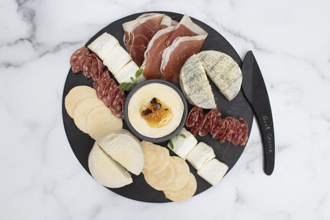 circular slate serving board with cheese and charcuterie