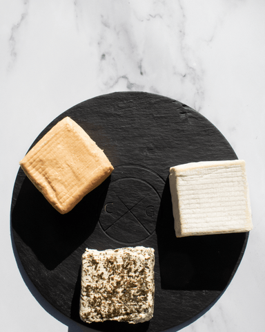 slate cheese serving board with three square cheeses on marble background