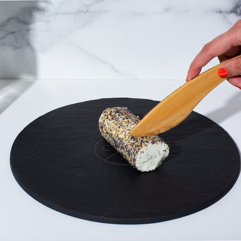 round black slate serving board with hand cutting into chevre cheese log with wooden knife