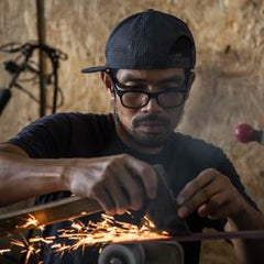 Thai blacksmith grinding an axe with sparks flying from the steel and grinder