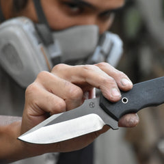 Knife maker holding up hand made SIam Blade knife. The knife is black with satin finish and maker's mark logo.