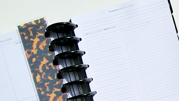 Discbound Jane's Agenda Planner opened to a daily page with the words daily vision practice written on the agenda and the opposite page is marked with a cheetah print page finder and 
