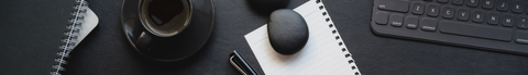 black desk with laptop, coffee, planner and notepad visible