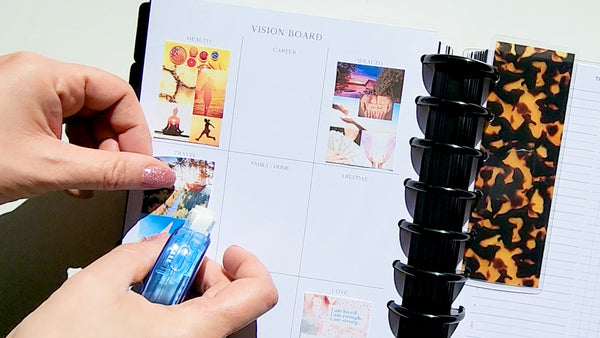 Woman's hands using an adhesive tape runner to adhere printed images to a Jane's Agenda Vision Board Insert