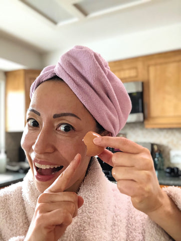 Woman in a robe, with turban, poinitng to an egg shell membrane, part of her DIY skin care routine