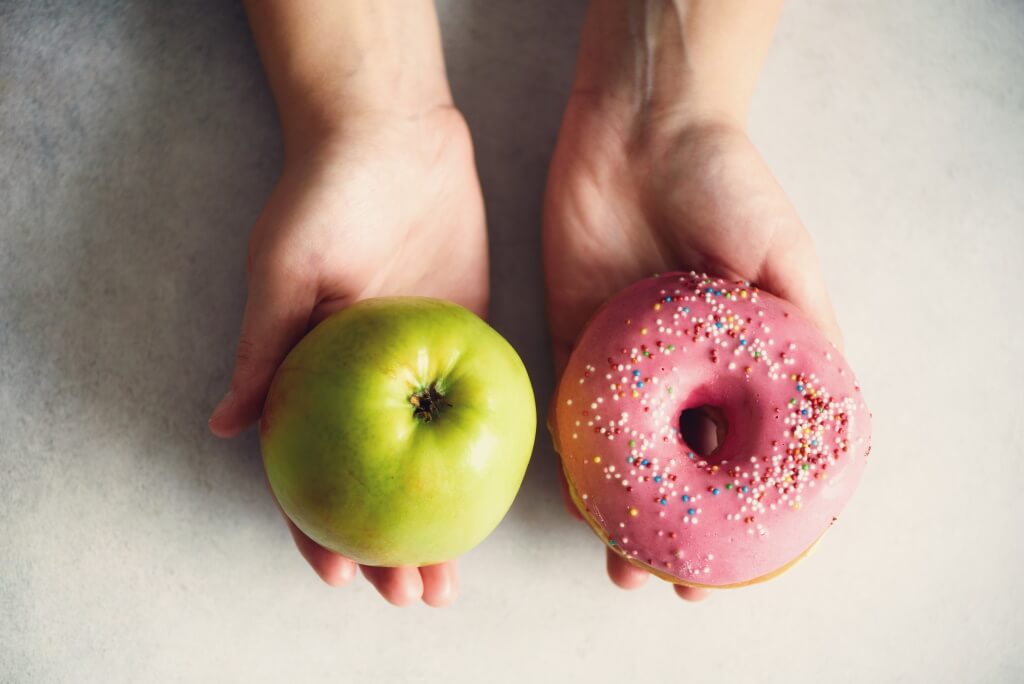 Le mani offrono una mela e una ciambella - la dieta influisce sul rischio di diabete
