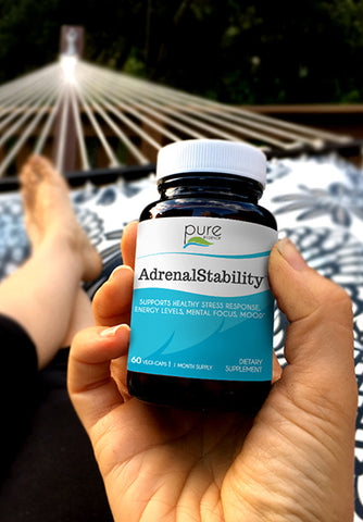 Woman's hand holding AdrenalStability product while relaxing on a hammock
