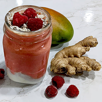 Ginger Mango Berry smoothie in a glass next to fresh ginger, raspberries, and mango