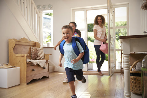 Boy and girl are happy running into the house after school, as mom holds the door open.