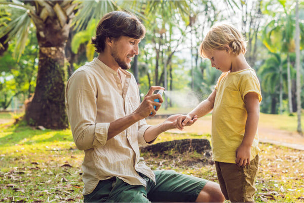 dad spraying child with natural bug repellent