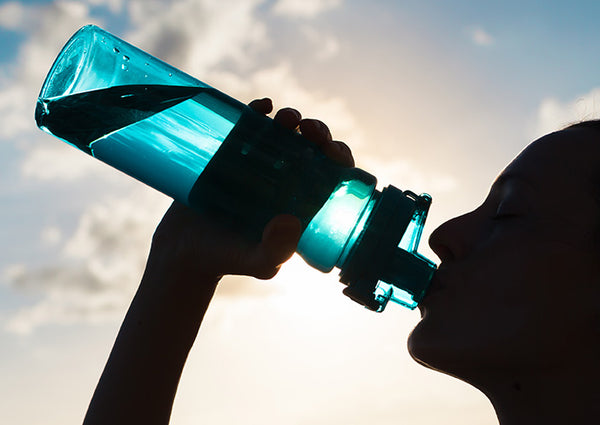 silhouette of a person drinking fluids from see-through water bottle