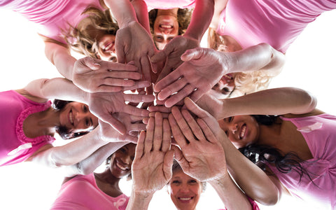 Ladies dressed in Pink gather in a circle with hands in to cheer for Breast Cancer Awareness support