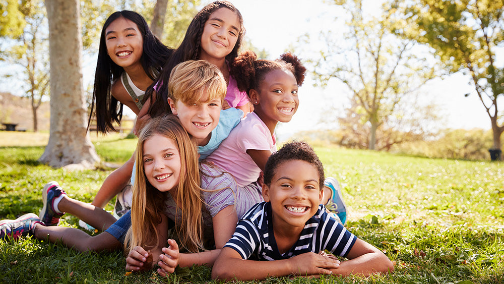 group of happy, healthy kids piled on top of one another while playing outdoors