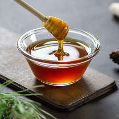 a honey dipper dripping into a bowl of honey