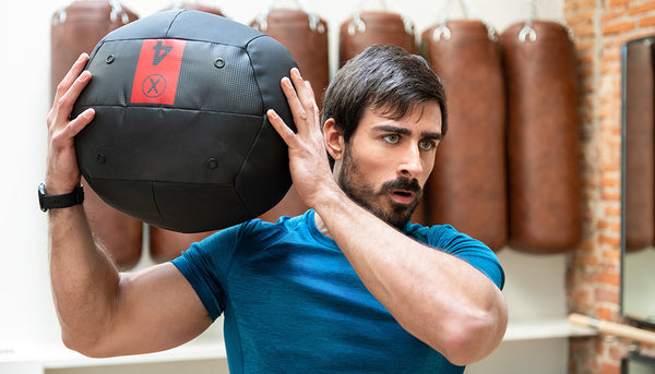 man focuses hard while doing intense exercise involving weighted ball