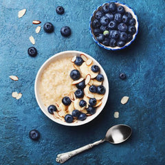 bowl of oatmeal topped with blueberries next to bowl of blueberries and a spoon