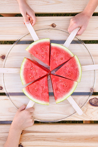 3 kid hands taking watermelon on popsicle sticks treats from plate