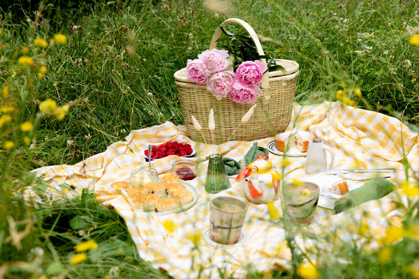 La Basketry handwoven picnic basket on a blanket surrounded by food and fresh flowers