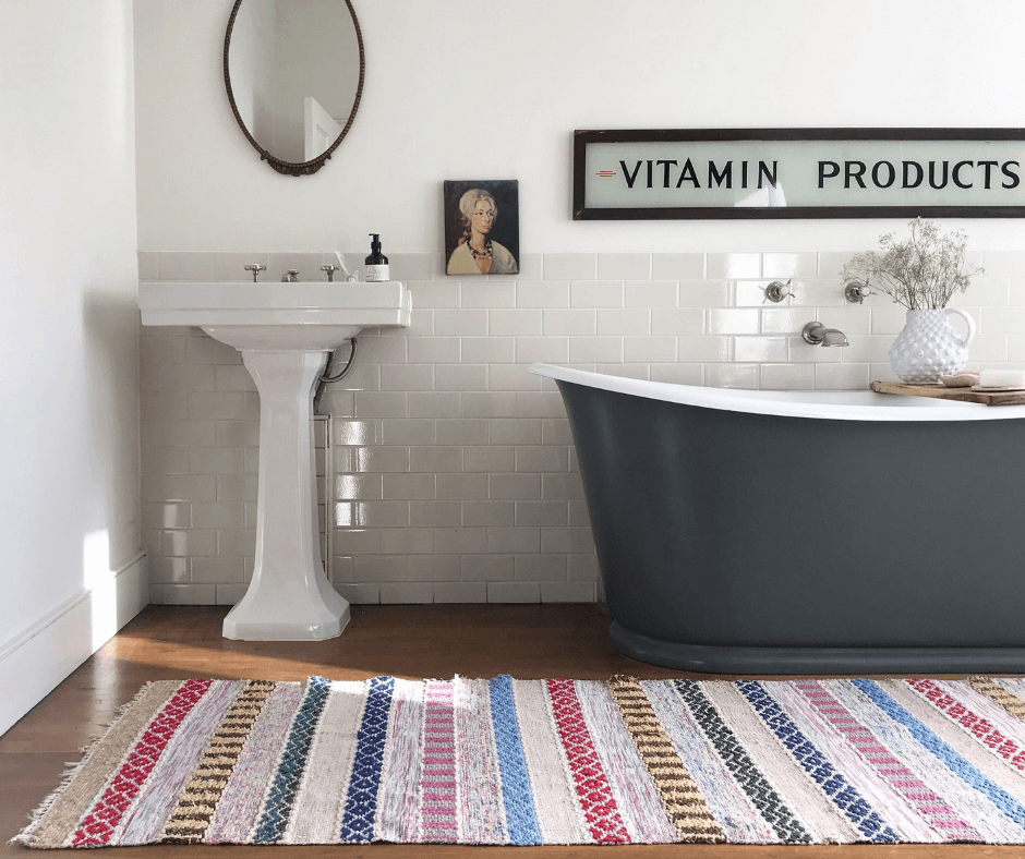 Deep grey bath tub in a white bathroom with a bright coloured striped rug from edit58 founded by Lisa Mehydene. Image for her interview with La Basketry