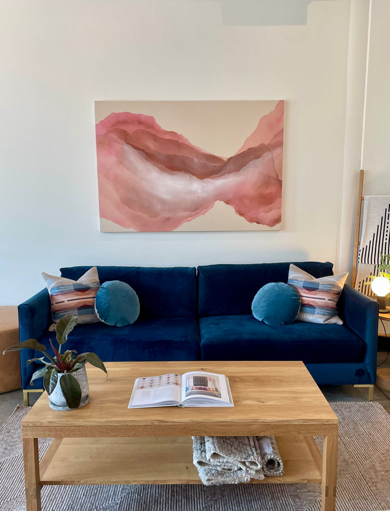 A navy blue velvet Charlie sofa is accessorized with Pendelton pillows by Bird Bird and a custom blush colored painting by Mandy Kav hangs above with an oak coffee table from the Joinery in front.