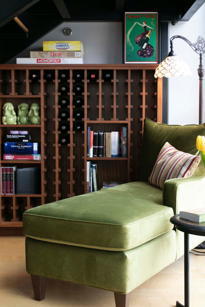 A soft green velvet chaise creates a cozy reading nook under the stairs