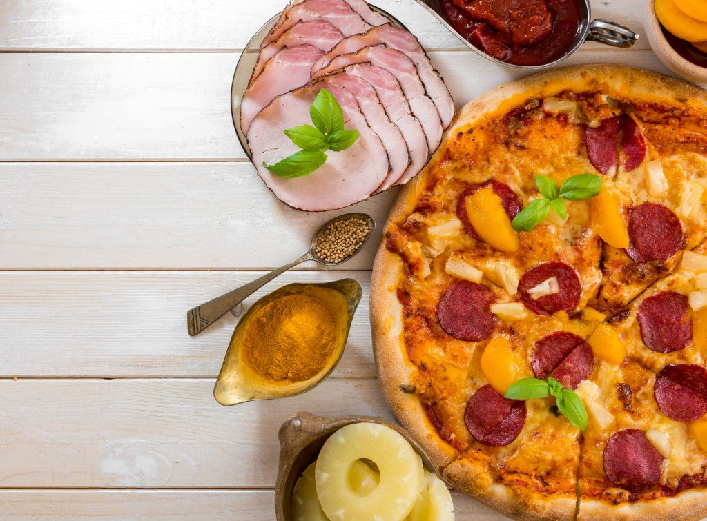 exotic pizza with pineapple and peach with food ingredients on a wooden table