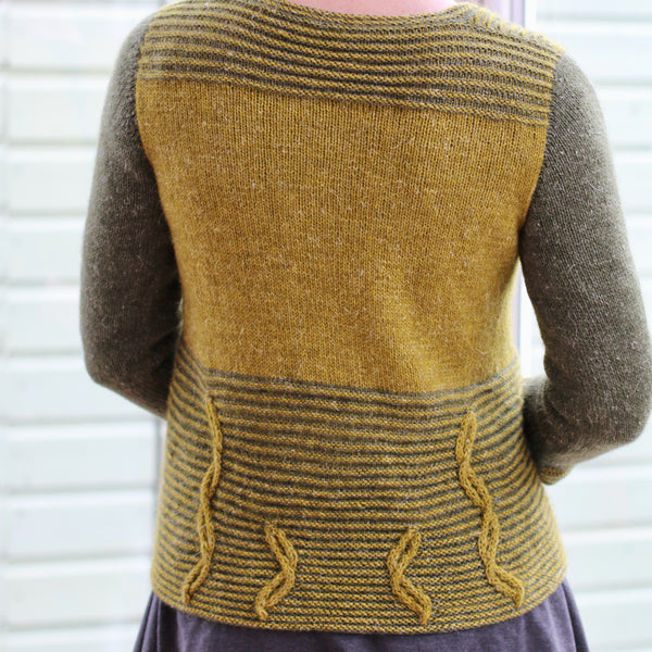 back of woman wearing laminarus cardigan in two shades of green with cables at the bottom of the body, 