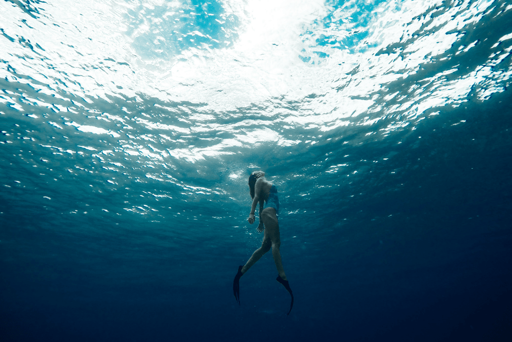 Freediving in the ocean wearing fins, mask and snorkel. Practicing to hold their breath while surrounded by beautiful coral reefs and ocean. 