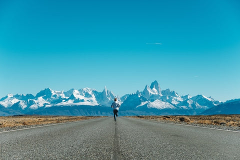 Male runner on empty road, snow-capped mountains in the background