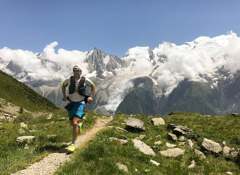 Trail runner on single track with snow-capped mountains in the background