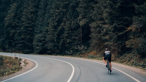 Cyclist on empty road approaching a turn, pine trees in background