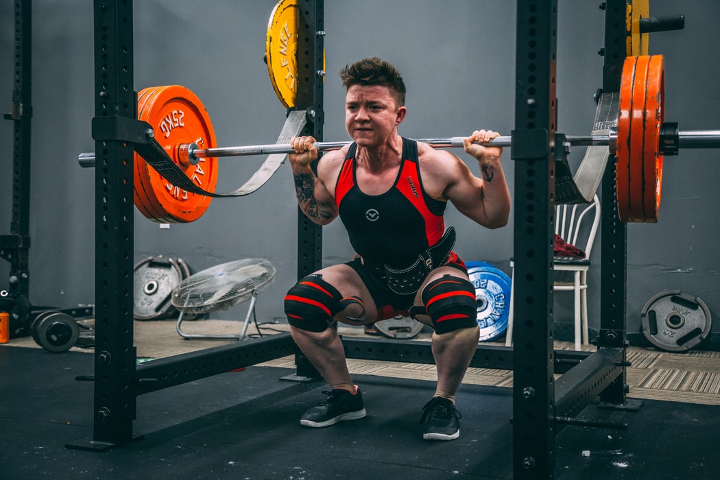 man wearing a black and red vest doing back squats in a gym