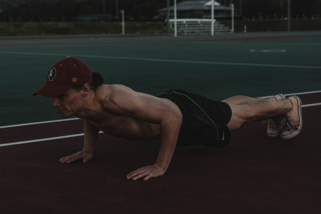 topless man doing push-ups at the side of a field