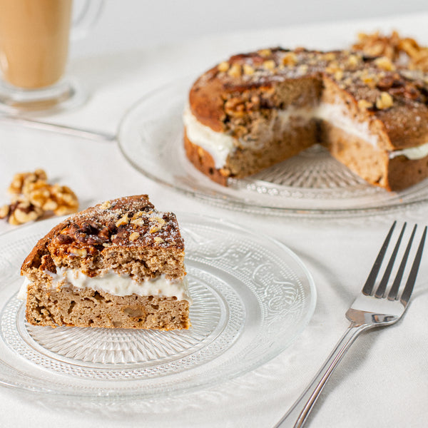 A slice of Lo-Dough coffee and walnut cake on a plate with the full cake in the background