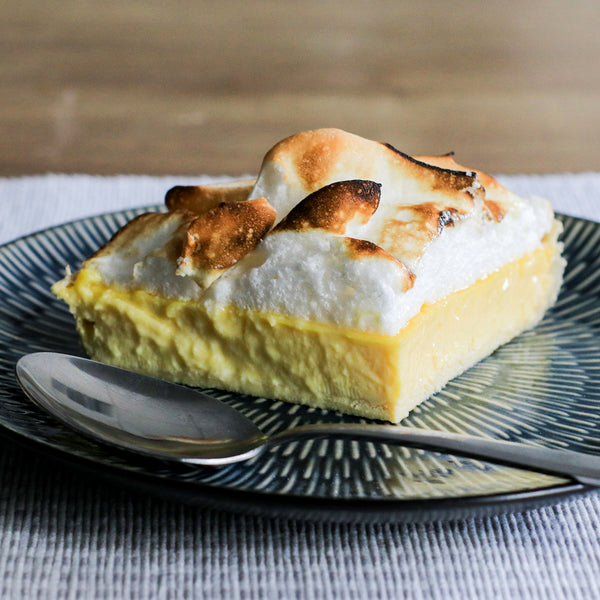 A slice of lemon meringue pie on a dark green plate with a spoon