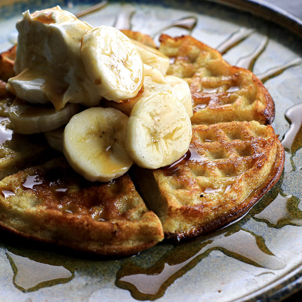 low calorie waffes on a dark plate with bananas and syrup on top 