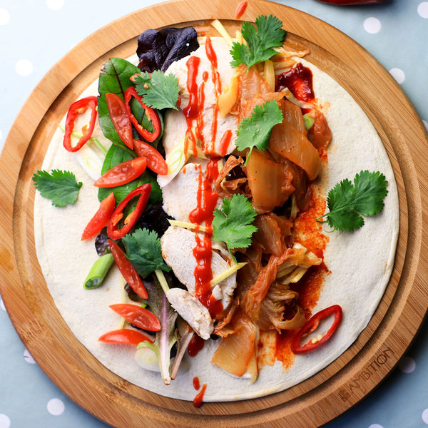 Chicken and kimchi Lo-Dough wrap on a circular wooden board