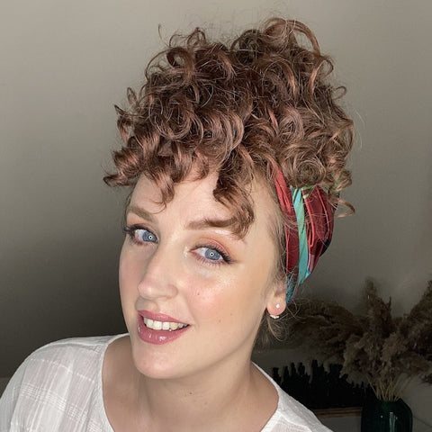 a woman smiles with her hair in a pineapple style and a headscarf