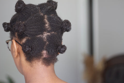 a woman wearing her type 4 hair in bantu knots faces away from the camera showing where her hair is parted