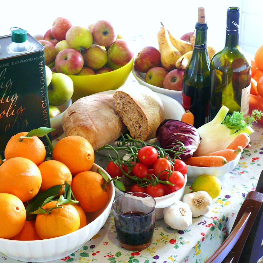Verschiedene Nahrungsmittel wie Orangen, Öl, Obst und Brot auf einem Tisch.